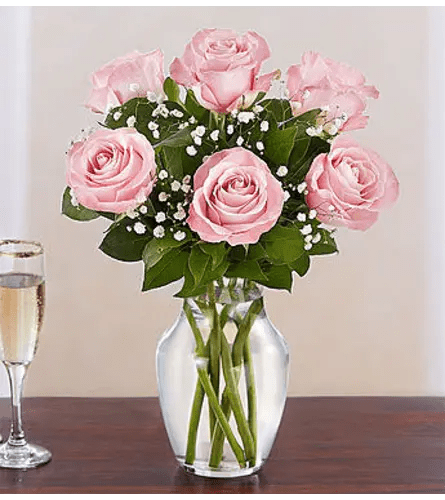 Pink roses with white filler flowers arranged in a clear glass vase on a table.