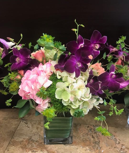 Purple orchids and pink hydrangeas in a square glass vase