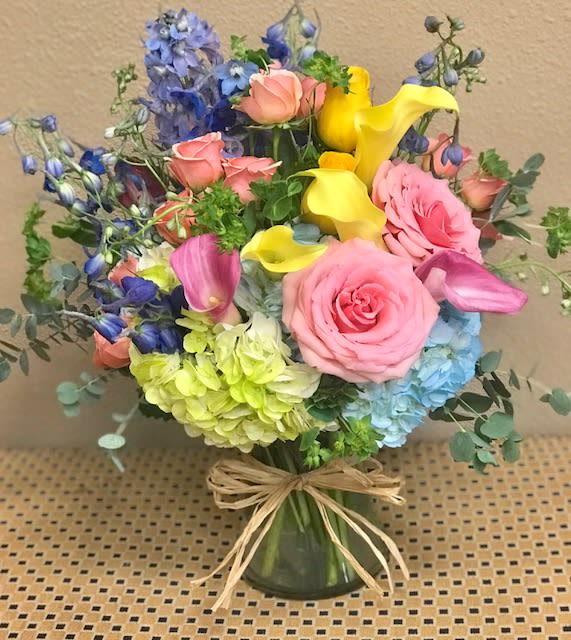Mixed bouquet with pink roses, yellow calla lilies, and blue flowers in a glass vase