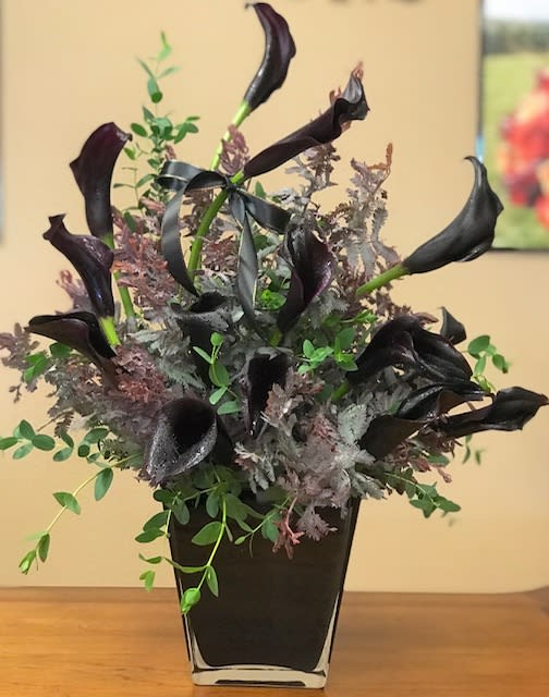 Black calla lilies in a square black vase with mixed greenery