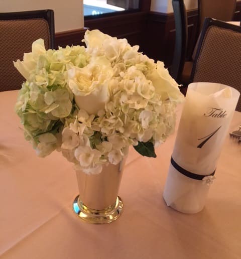White floral centerpiece in a tall vase beside a rolled napkin