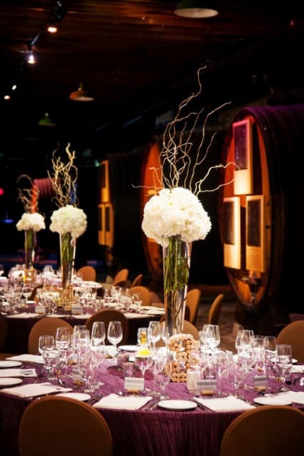 Tall white floral centerpieces on banquet tables in a dim event hall
