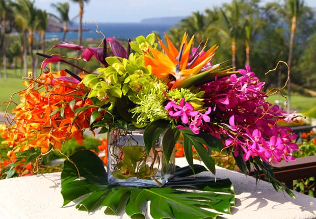 Tropical flower arrangement in a glass cube vase with orange, pink, and green blooms