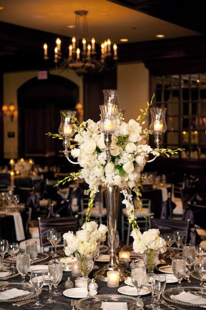 White floral centerpiece with candles in tall glass holders on a banquet table