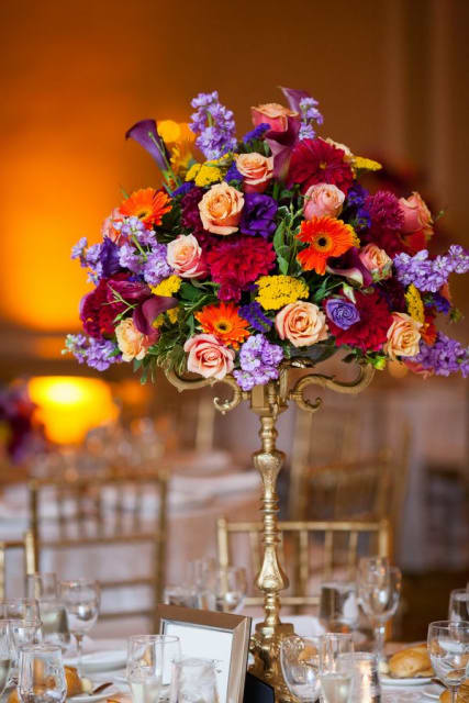 Tall floral centerpiece with roses, calla lilies, and gerbera daisies in a gold stand