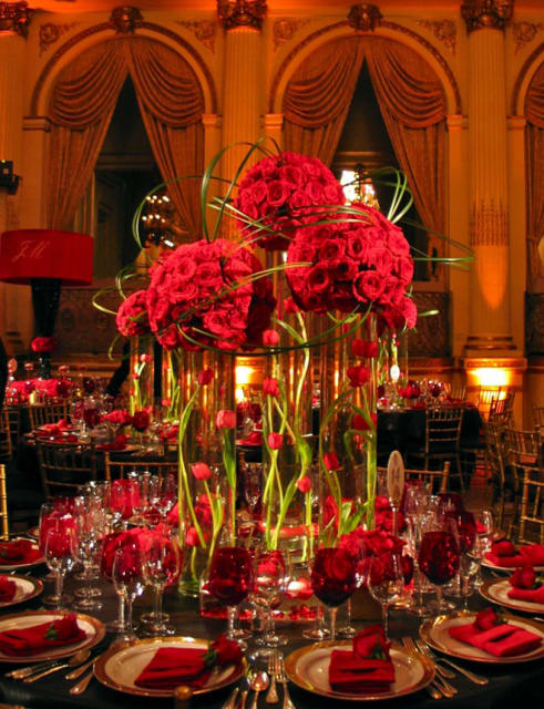 Tall red rose centerpieces in glass vases on a formal banquet table