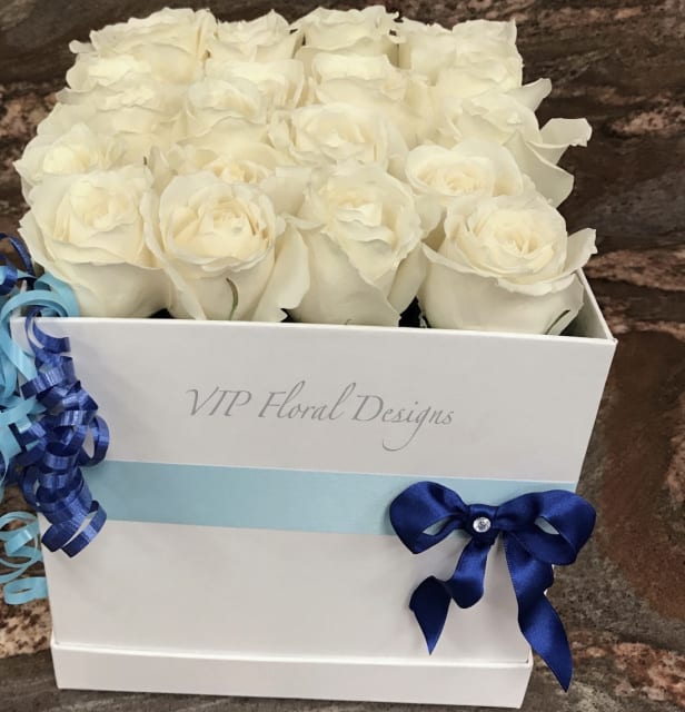 White roses arranged in a white gift box with blue ribbon accents.