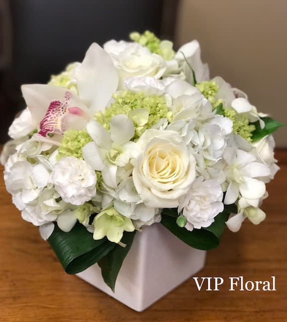 White floral arrangement in a square vase with pale green accents