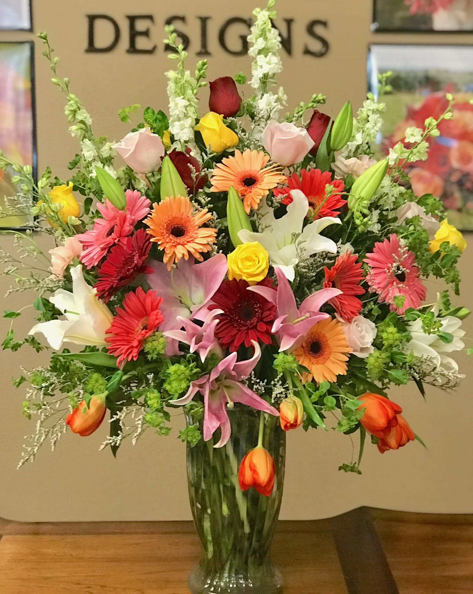 Mixed bouquet of roses, lilies, and gerbera daisies in a tall glass vase