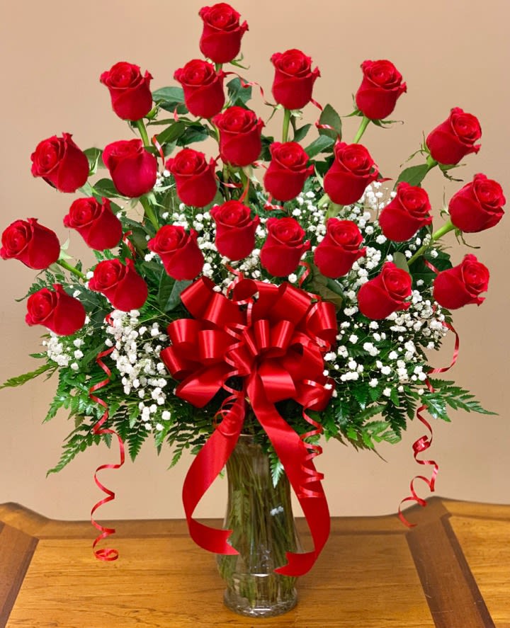 Red roses arranged in a clear glass vase with a large red bow