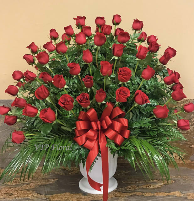 Large arrangement of red roses in a white urn with a red ribbon bow