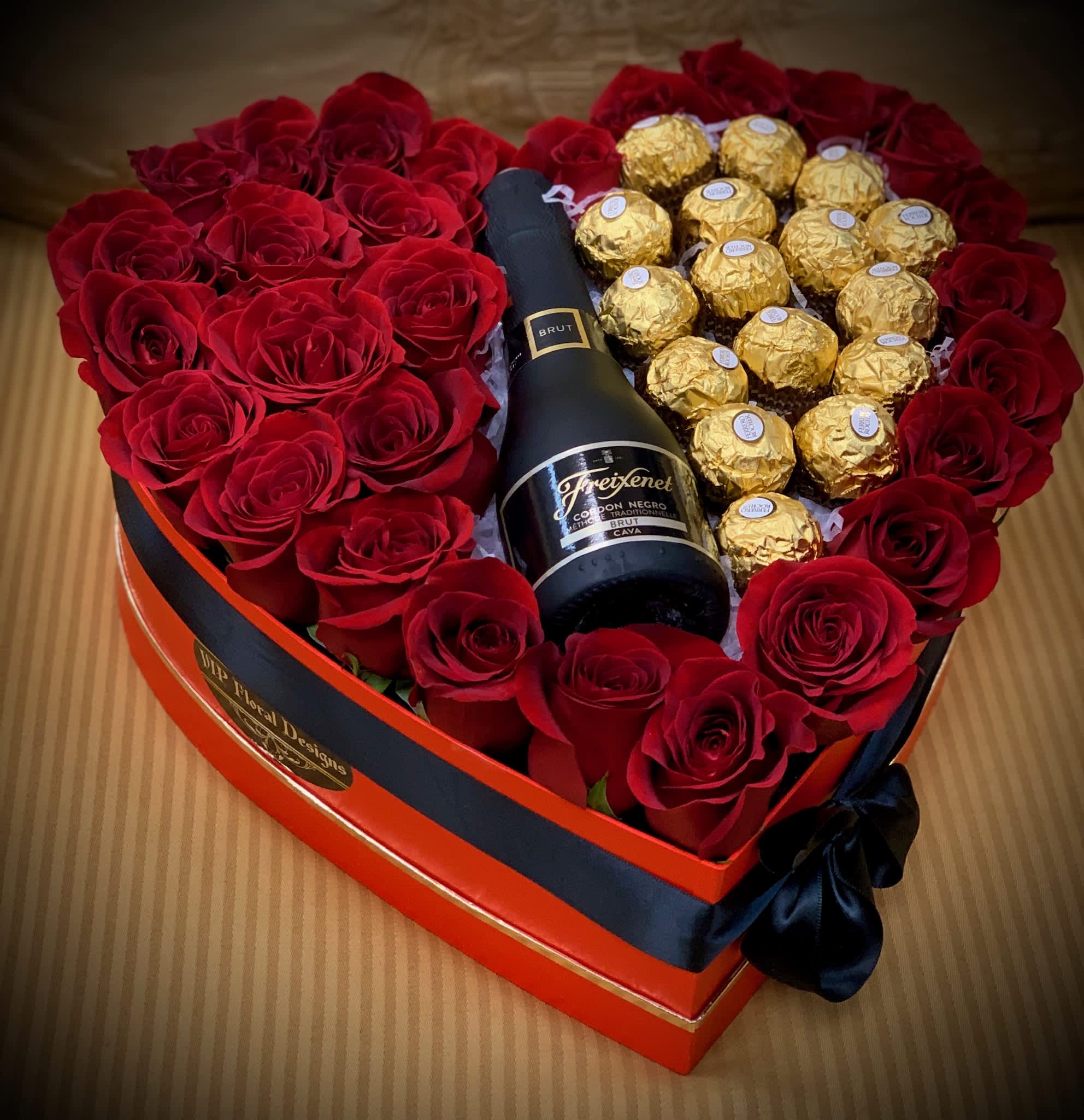 Heart-shaped box with red roses, gold chocolates, and a champagne bottle
