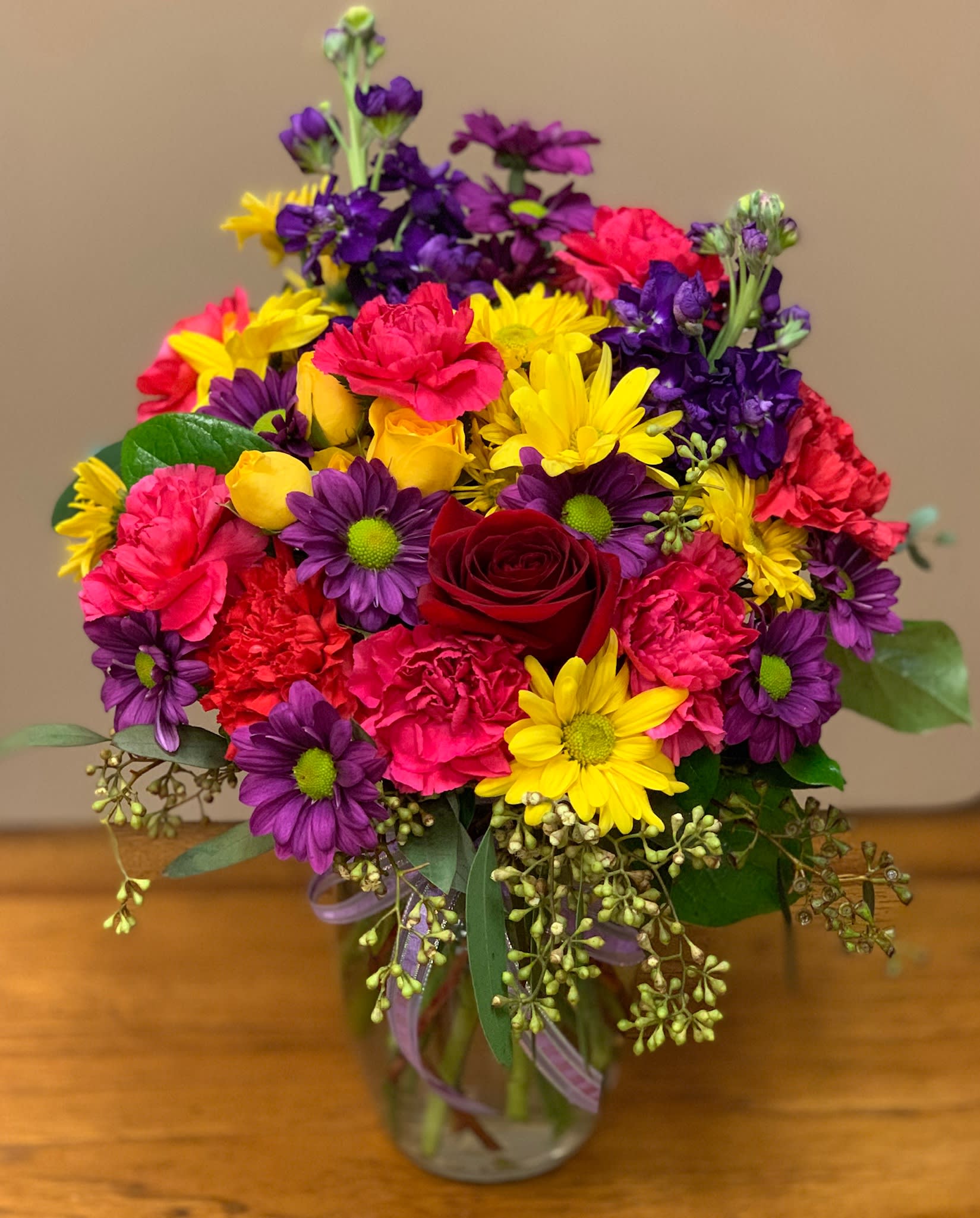 Colorful bouquet of daisies, carnations, and a red rose in a glass vase