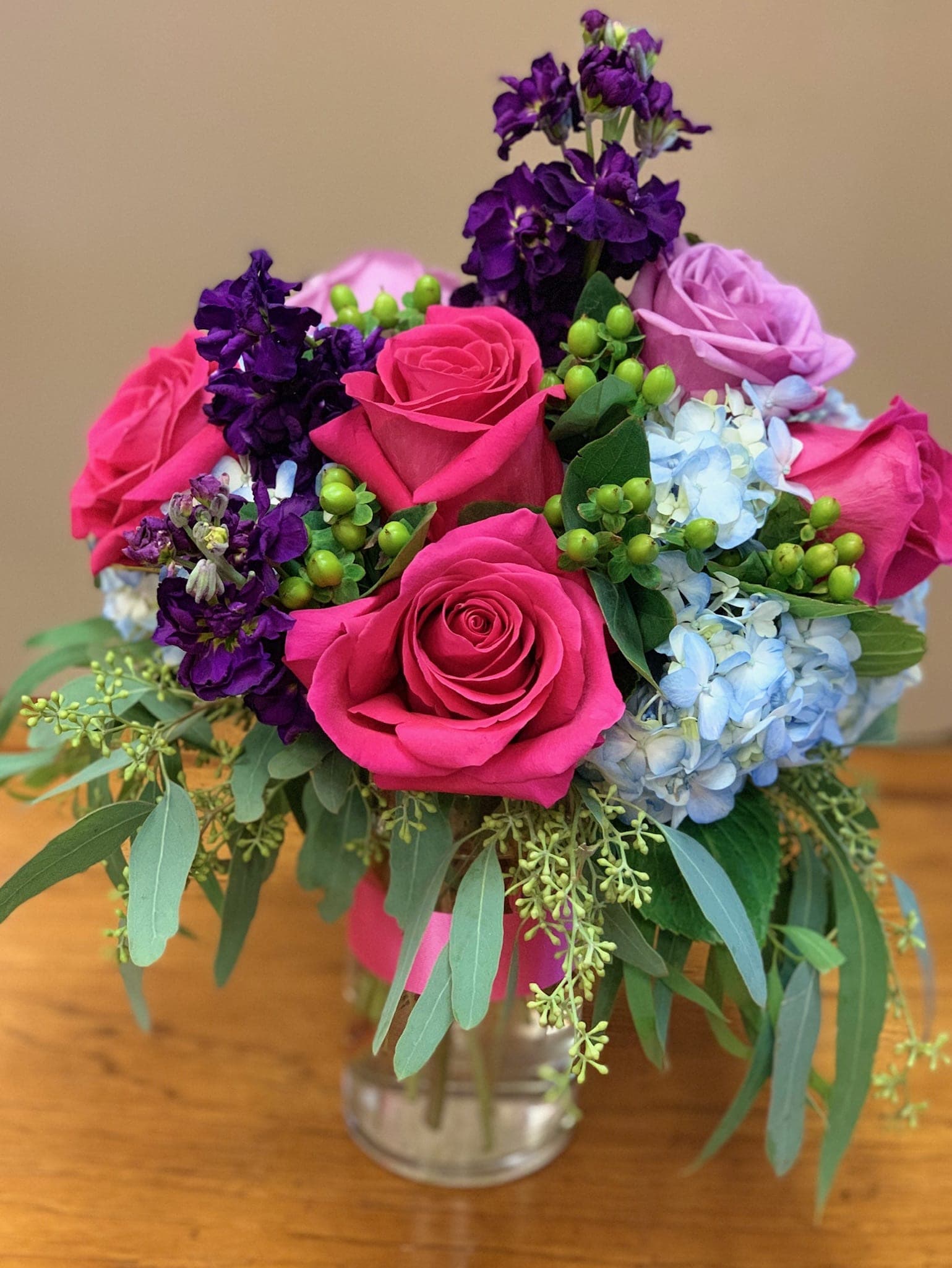 Bouquet of pink roses, purple blooms, and blue hydrangeas in a glass vase