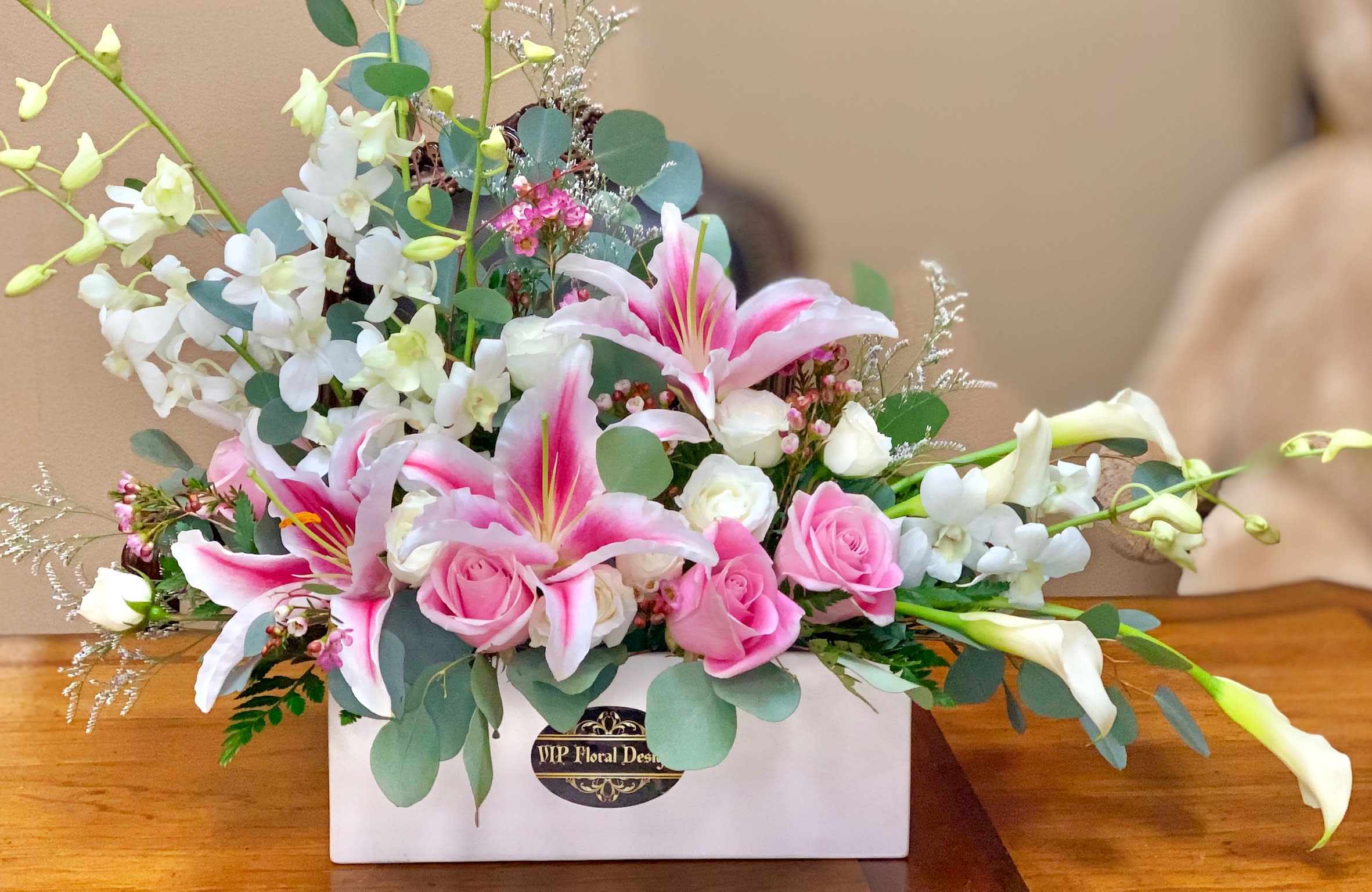 Pink lilies and roses arranged in a white box with white orchids