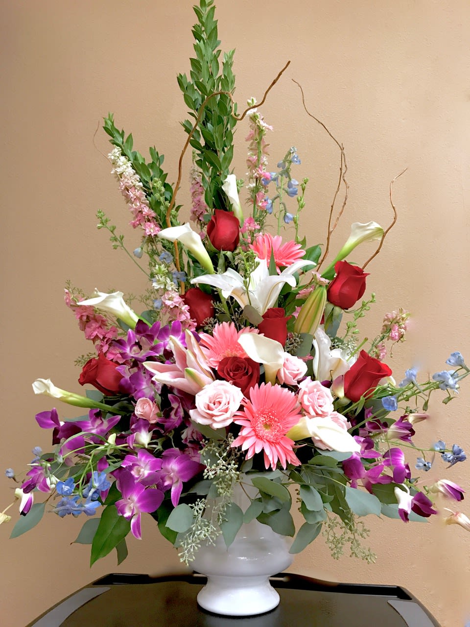 Large mixed bouquet of roses, lilies, orchids, and gerbera daisies in a white vase