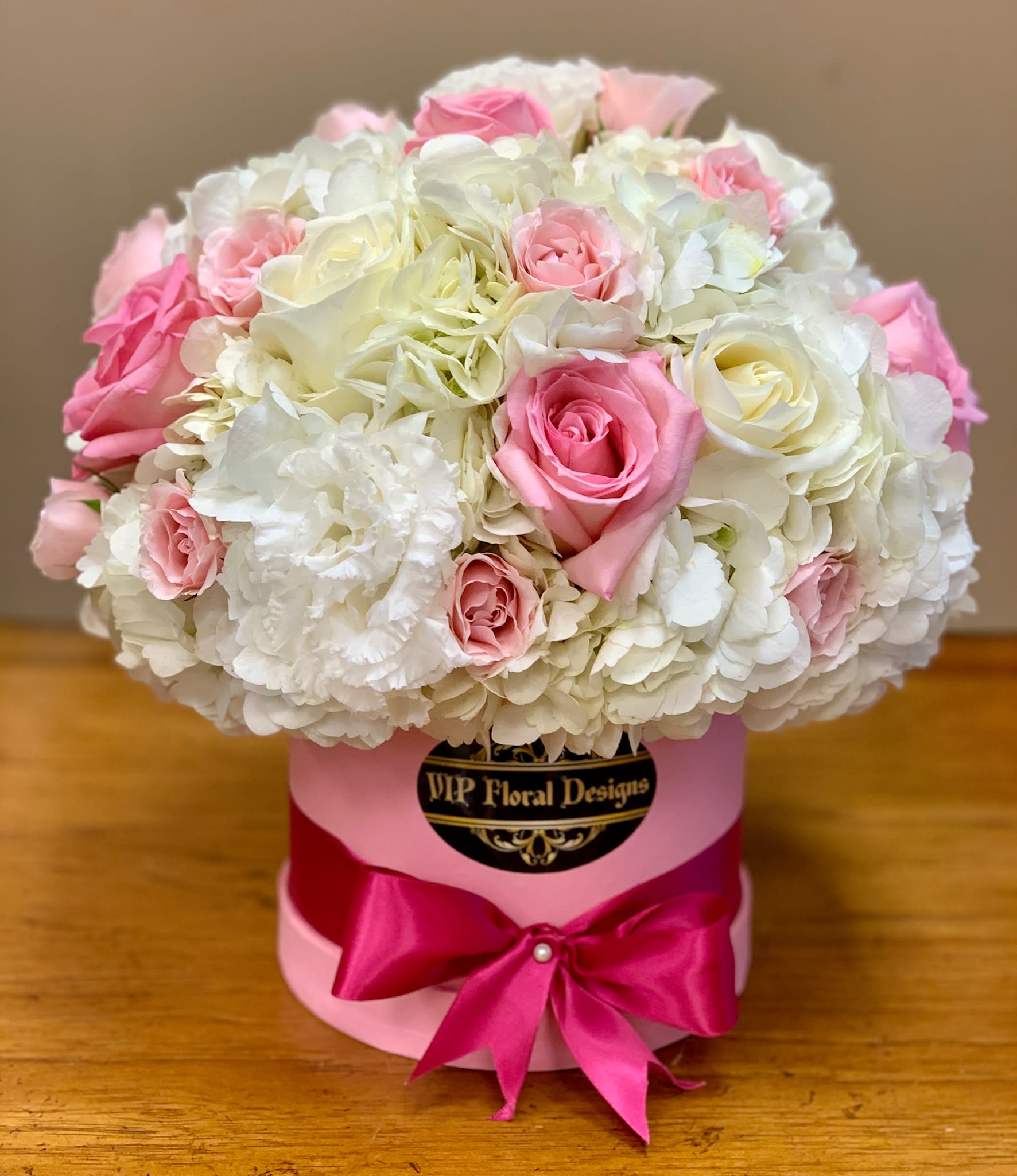 Pink and white roses arranged in a round hat box with a satin bow