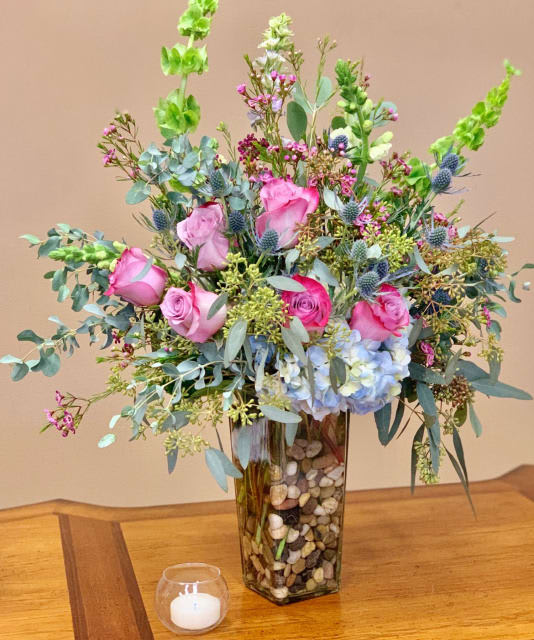 Pink roses and blue hydrangea in a tall glass vase with pebbles