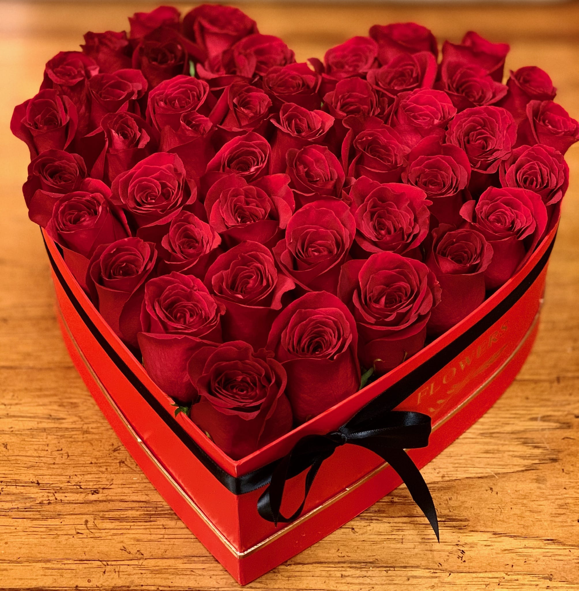 Heart-shaped box filled with red roses and tied with a black ribbon