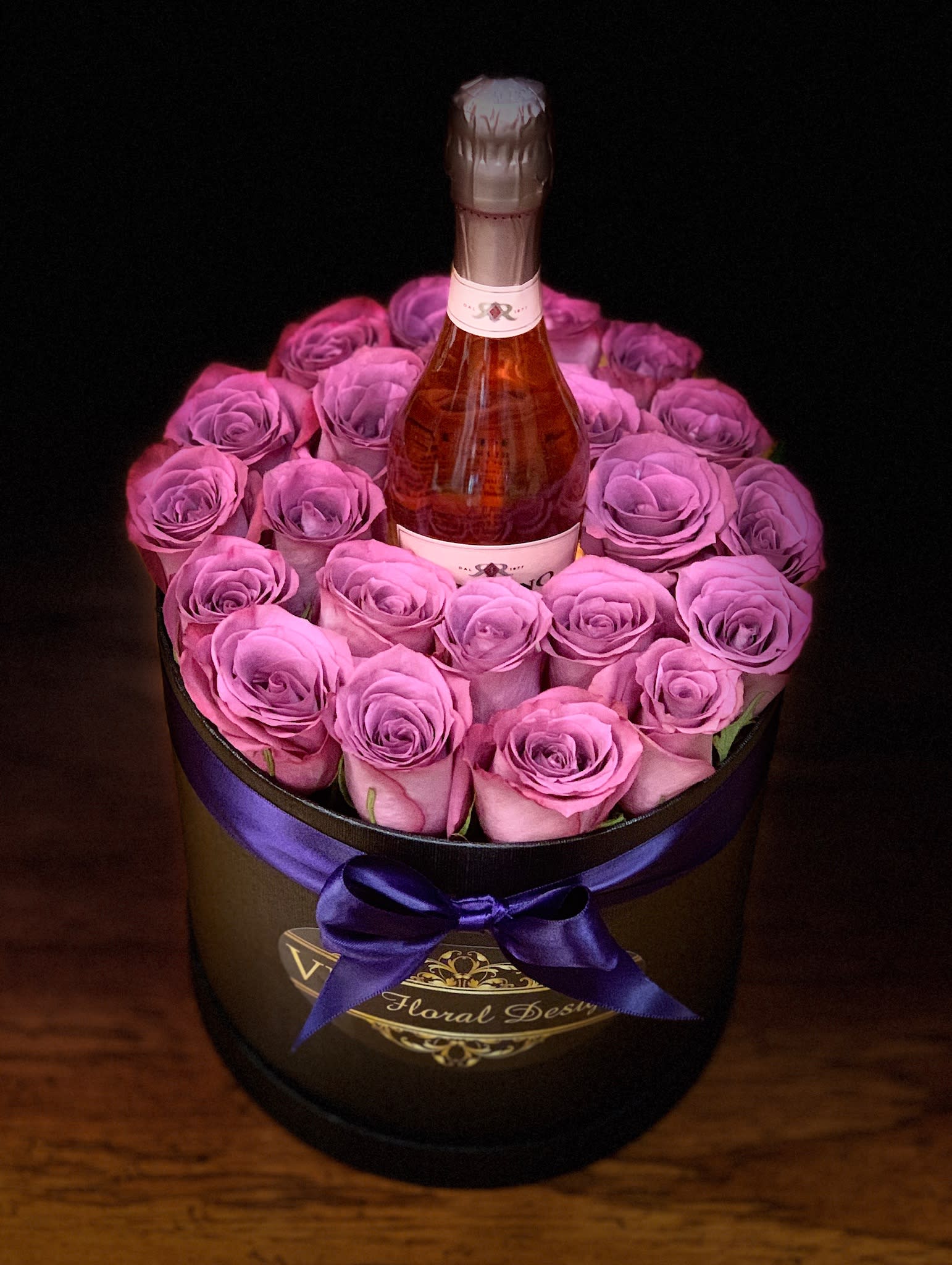 Pink roses arranged around a champagne bottle in a round box