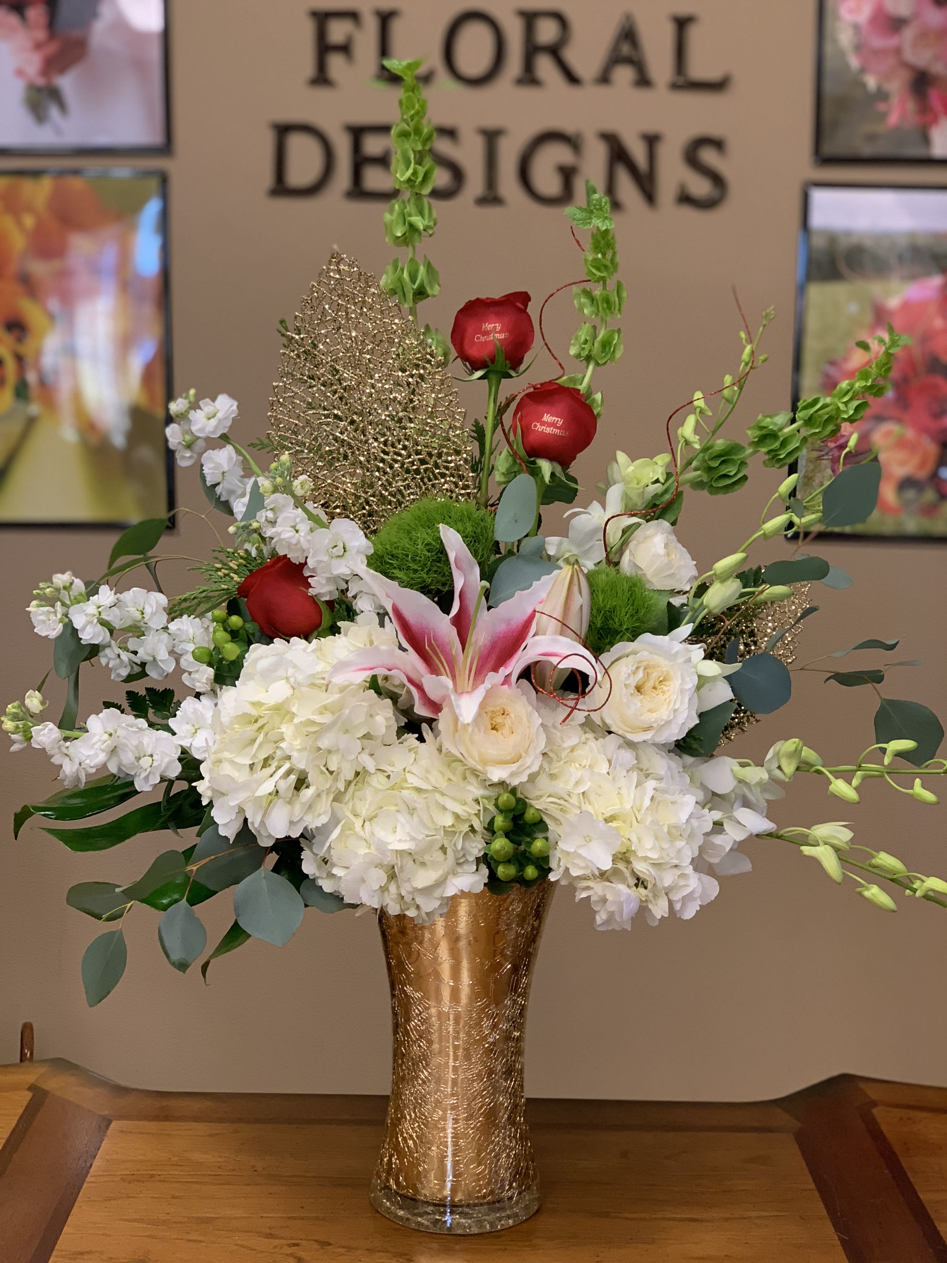 Tall floral arrangement with white blooms, red roses, and pink lilies in a gold vase