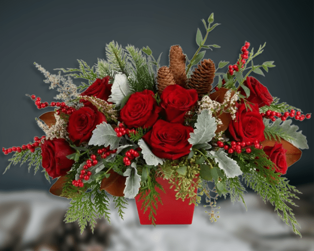 Red roses arranged in a red container with pinecones and berries