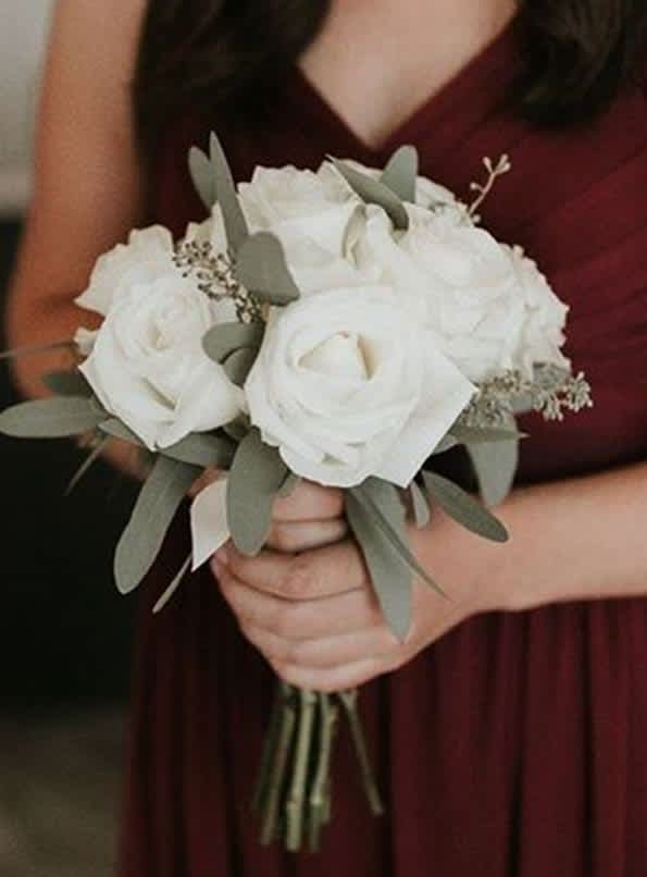 White rose bouquet with eucalyptus held by a person in a burgundy dress