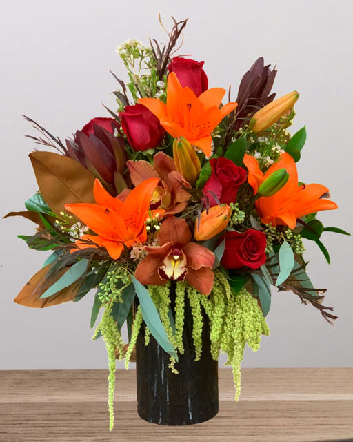 Bouquet of orange lilies and red roses in a black vase