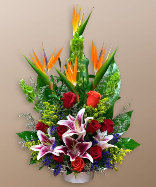 Tropical bouquet with red roses and pink lilies in a white container