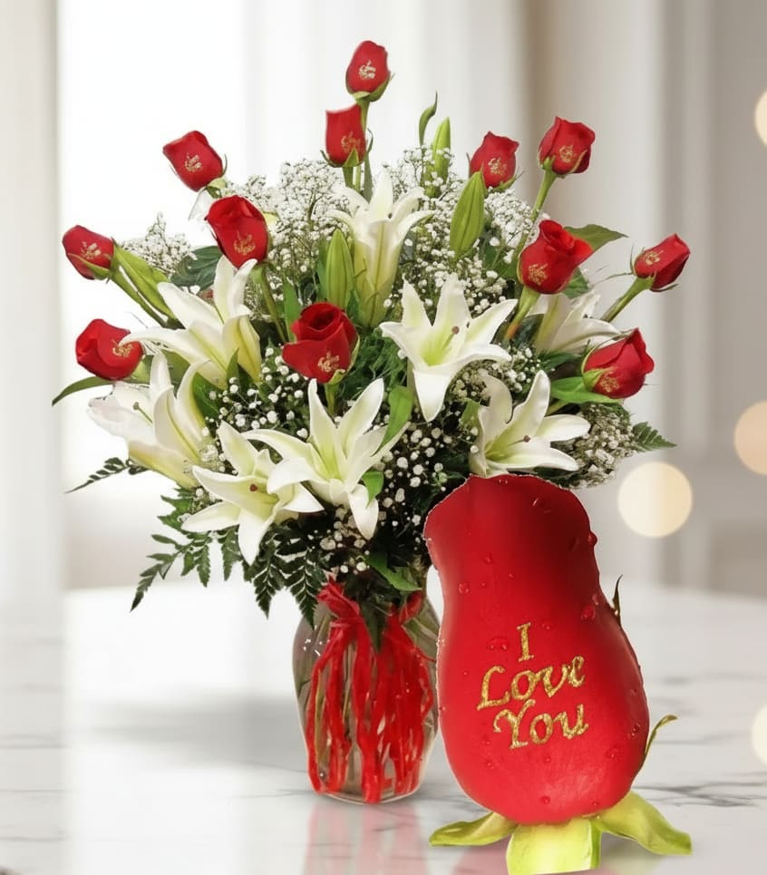 Red roses and white lilies in a glass vase beside a red rose-shaped gift