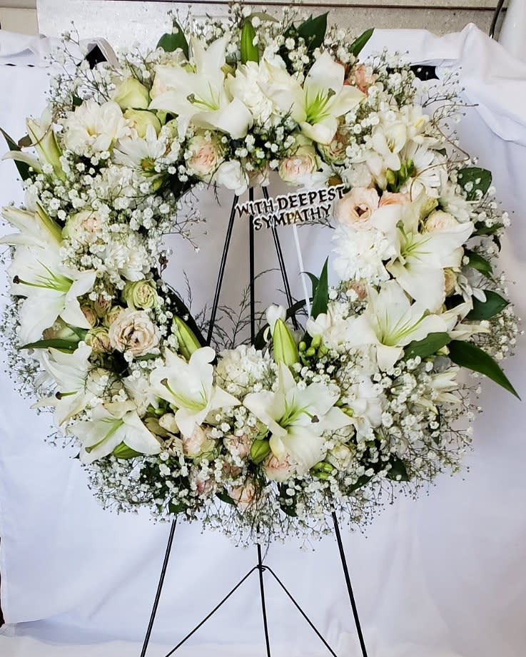 White sympathy wreath on a black stand with lilies and roses