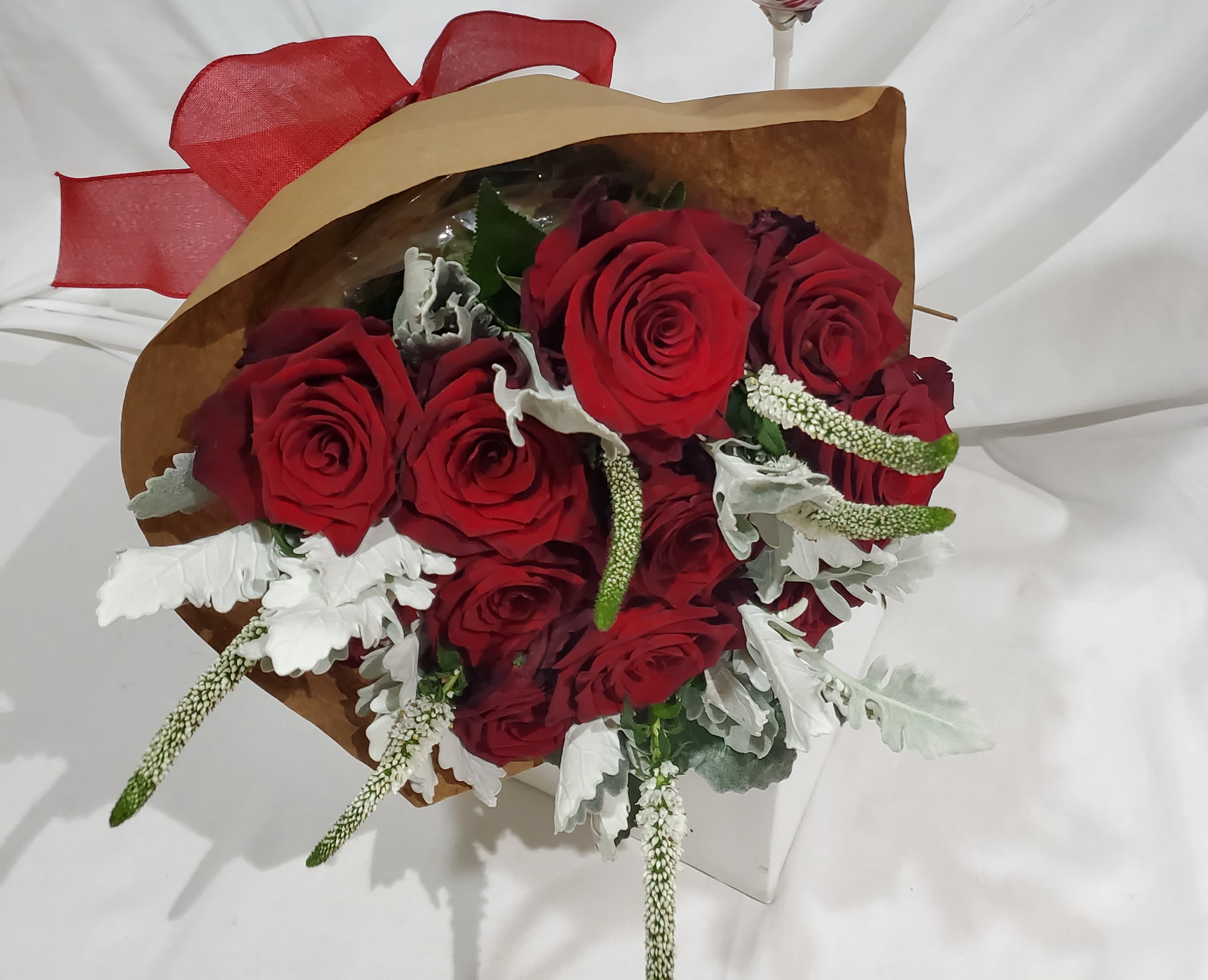 Bouquet of red roses with white filler flowers wrapped in brown paper and red ribbon