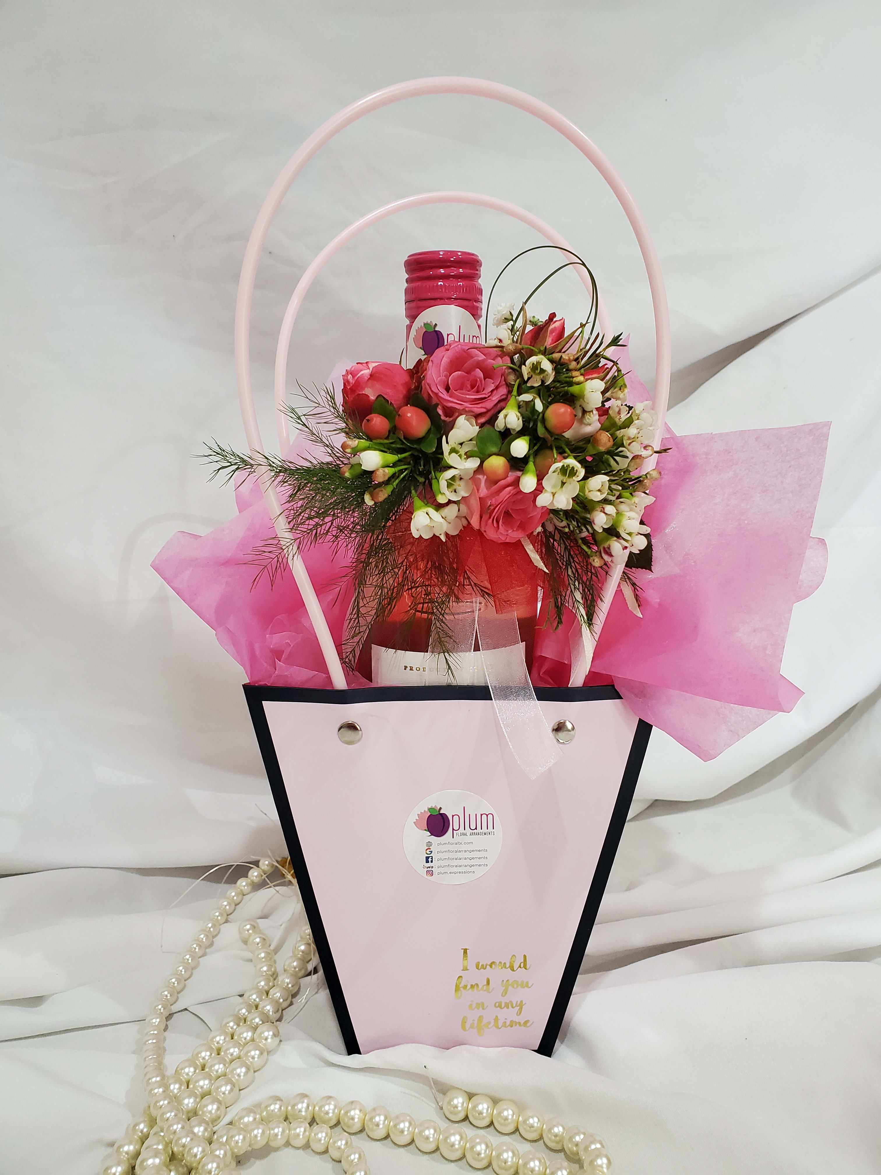 Pink rose arrangement in a gift bag with a bottle and pearl strands