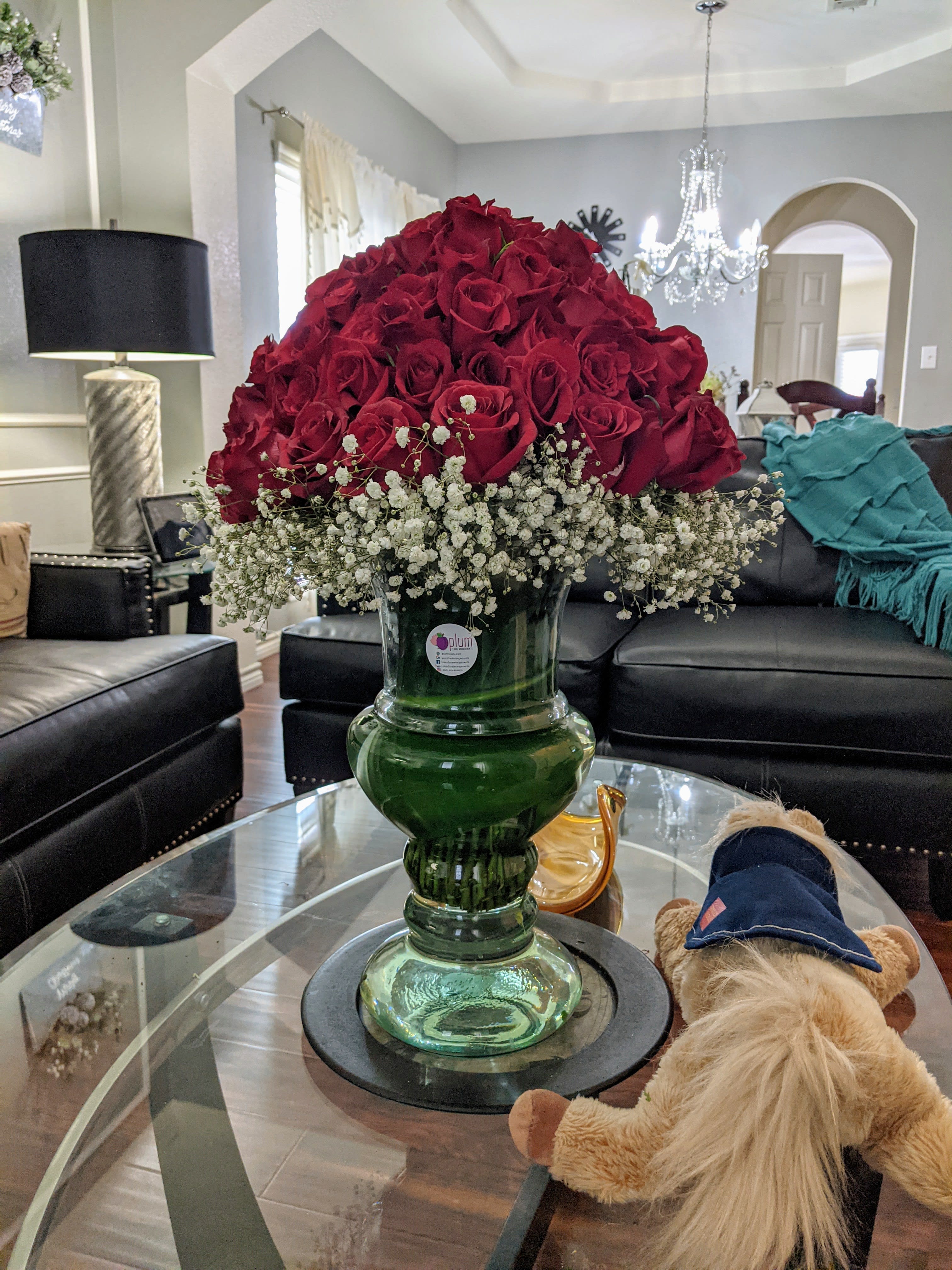 Large red rose arrangement in a green glass vase with white baby's breath
