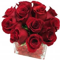Red roses arranged in a clear square glass vase.