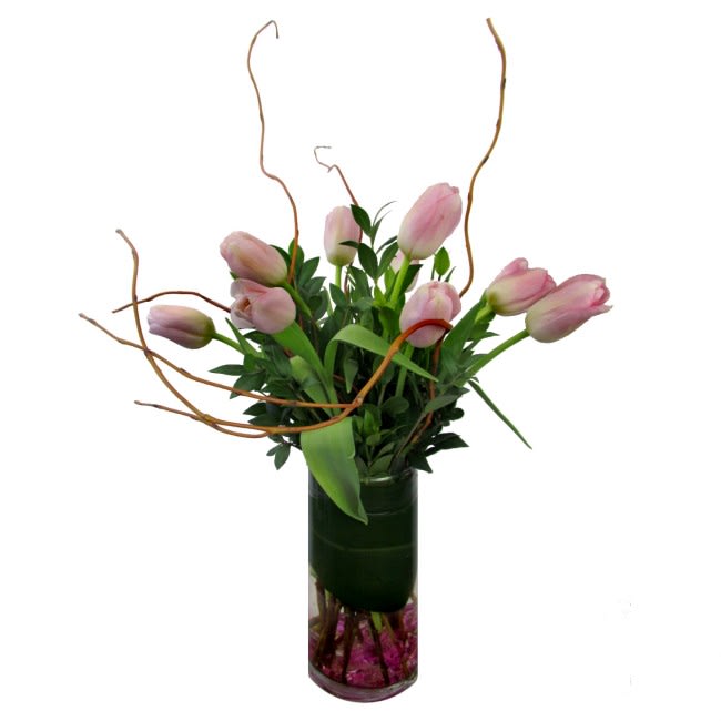 Pink tulips arranged in a tall glass vase with curly branches