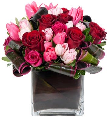 Bouquet of pink and red roses and tulips in a square glass vase