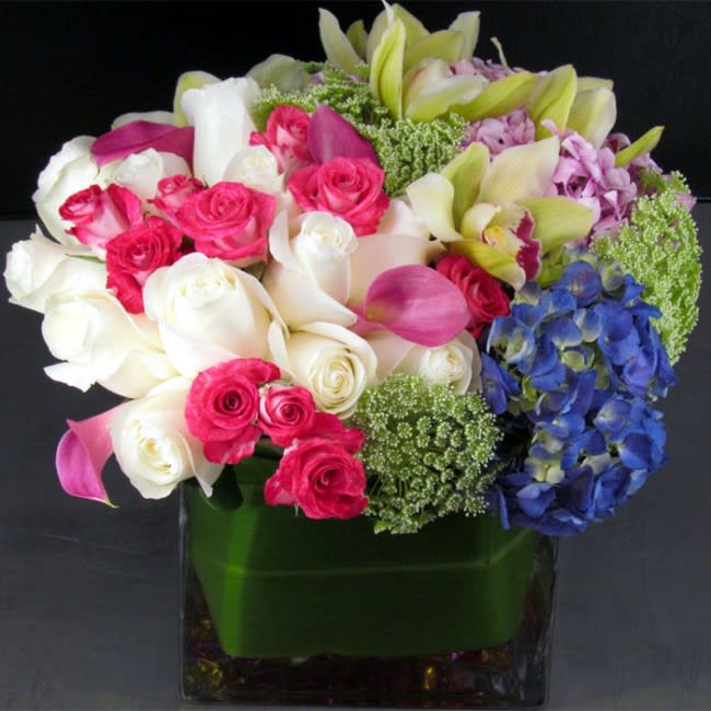 Mixed bouquet of roses, calla lilies, orchids, and hydrangea in a glass vase