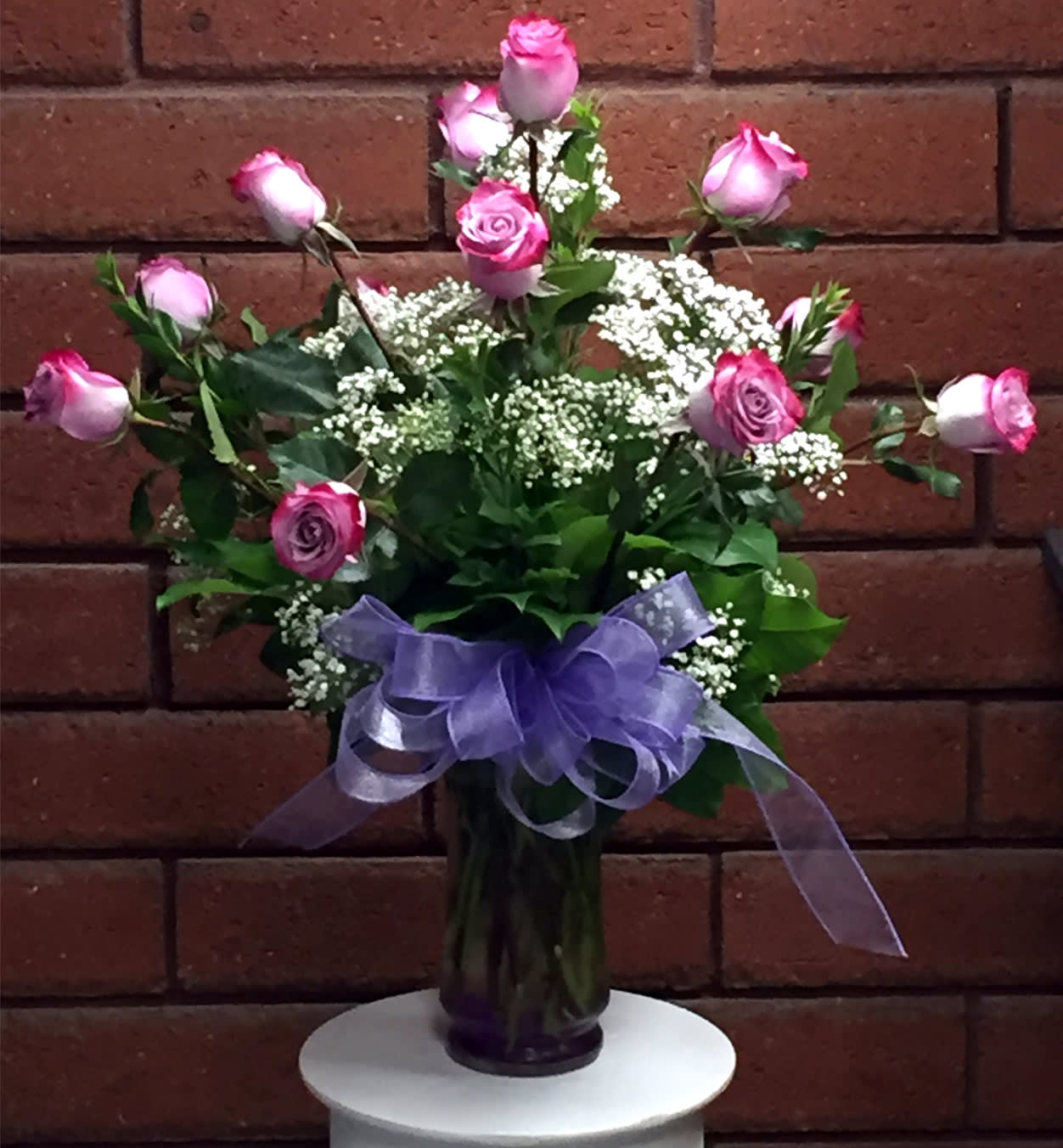 Pink roses in a glass vase with a purple ribbon