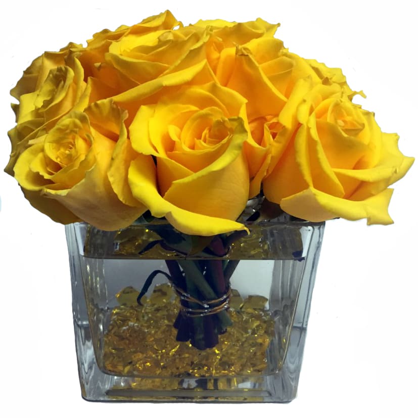 Yellow roses arranged in a clear square vase with decorative stones