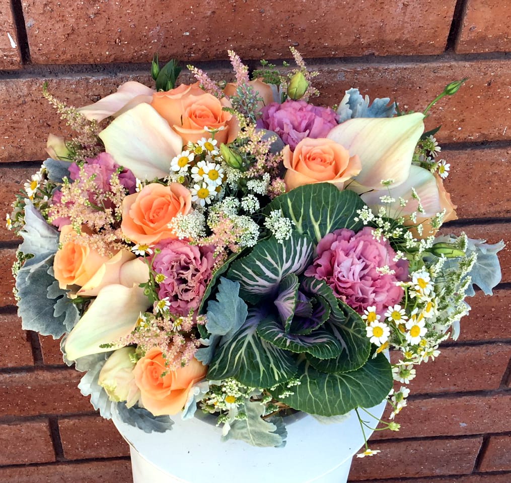 Bouquet of peach roses, pink blooms, and white calla lilies in a white container