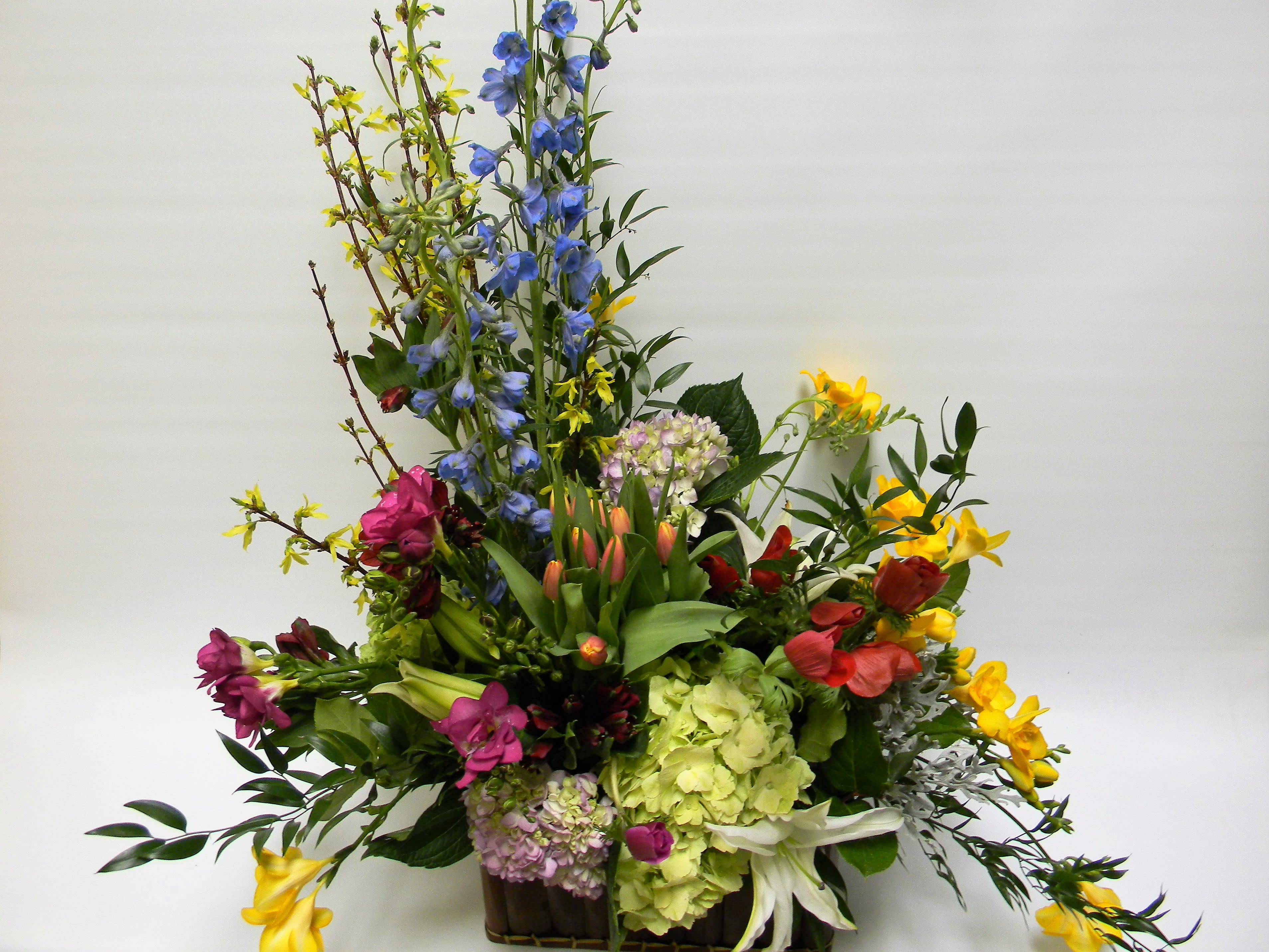 Tall mixed flower arrangement with blue, yellow, pink, and green blooms in a container