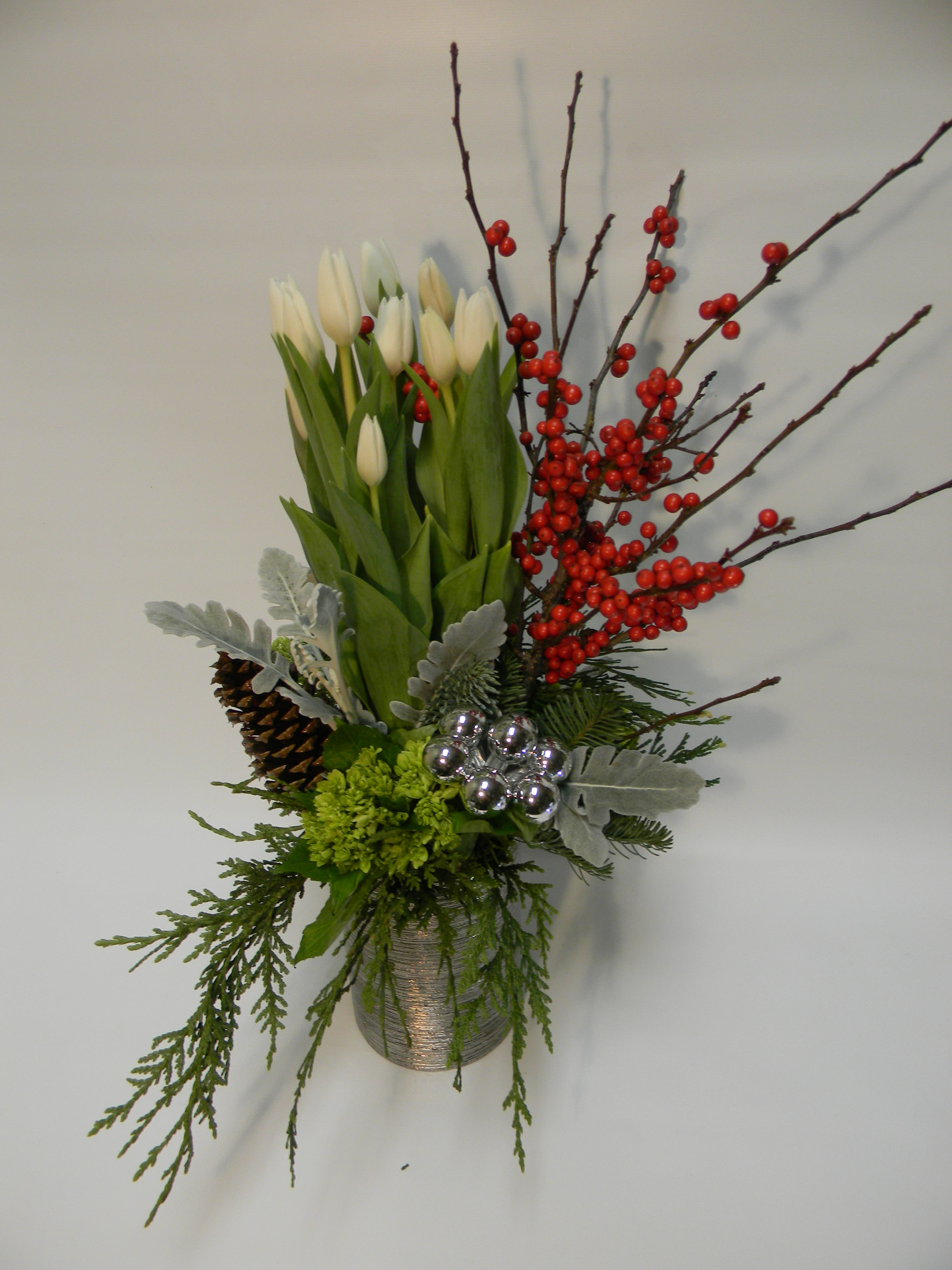 White tulips in a silver vase with red berries and pinecones
