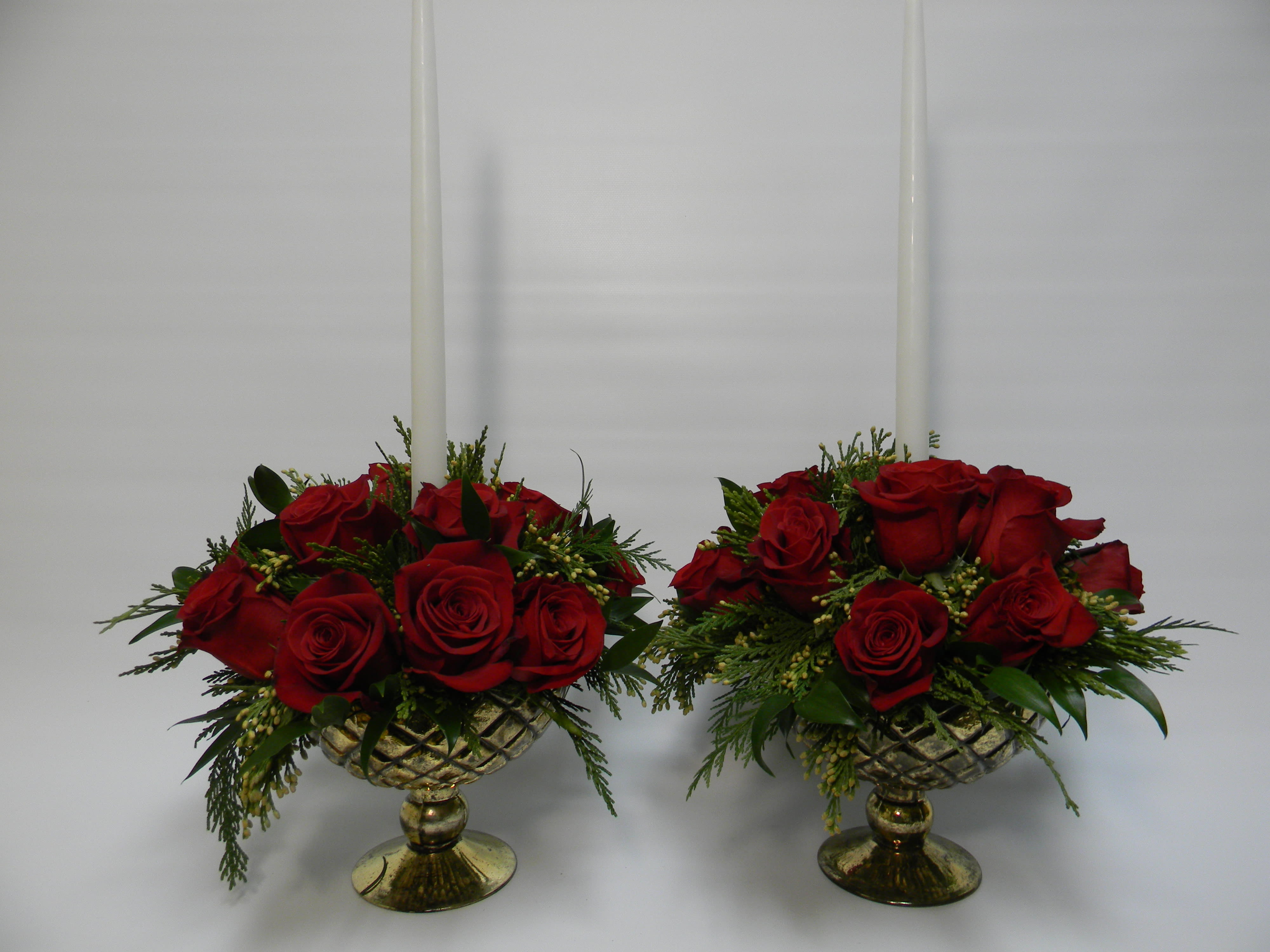 Two red rose arrangements in gold pedestal bowls with tall white candles