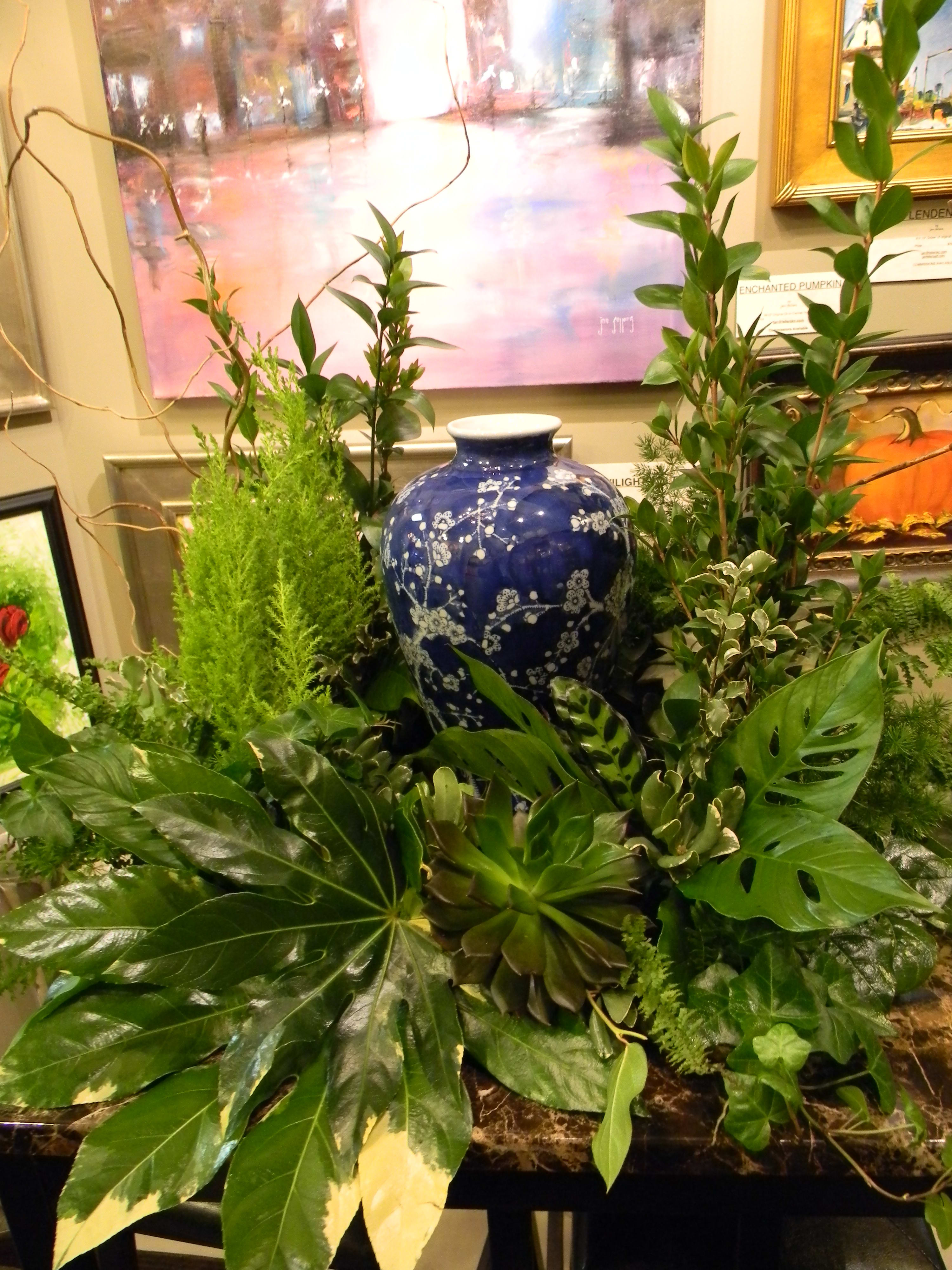 Lush green plant arrangement around a blue ceramic vase