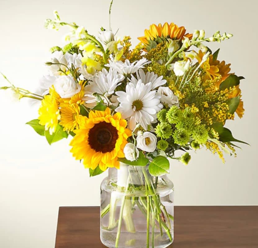 Bouquet of sunflowers, white daisies, and yellow flowers in a glass vase