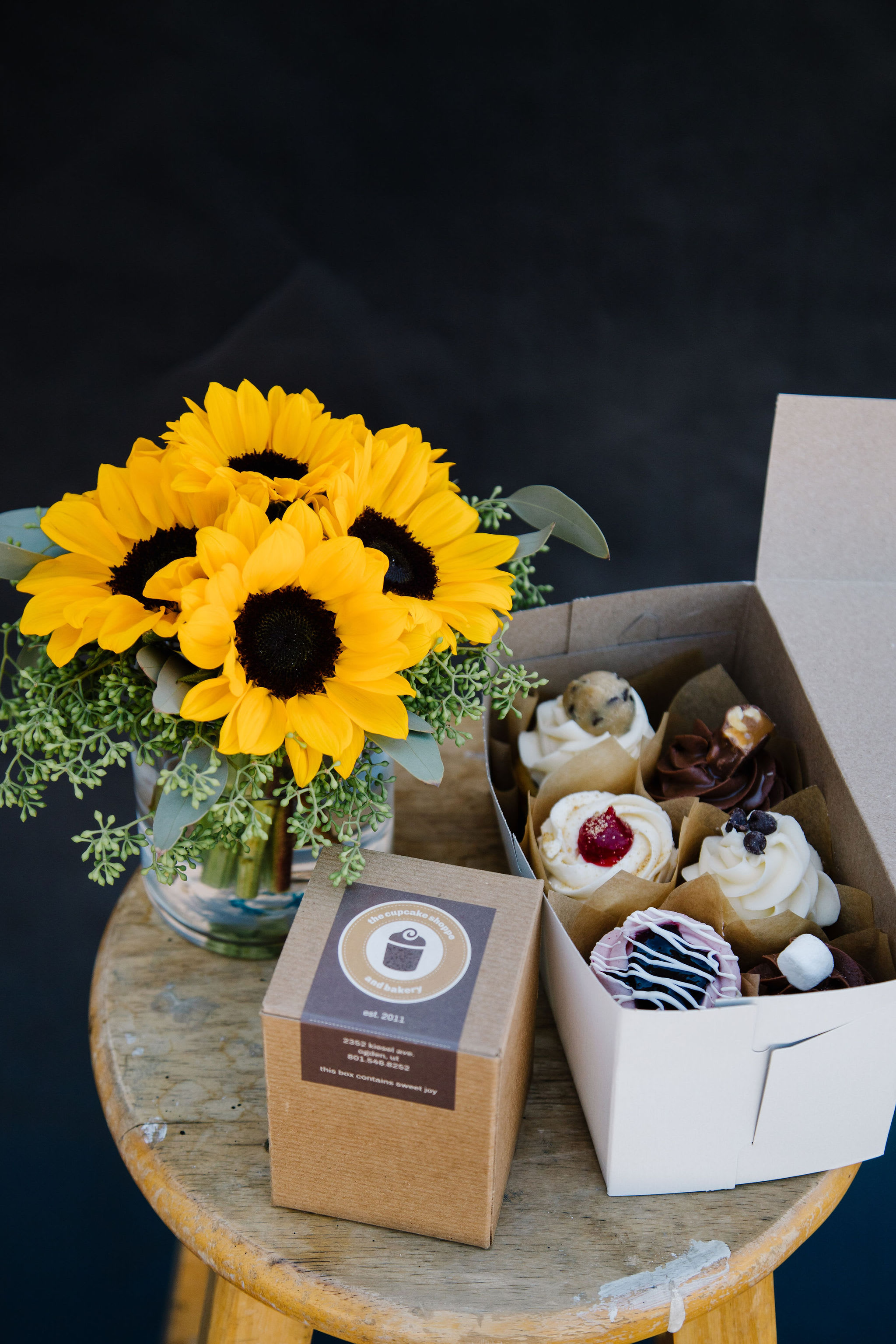 Sunflower bouquet in a glass vase beside a box of cupcakes