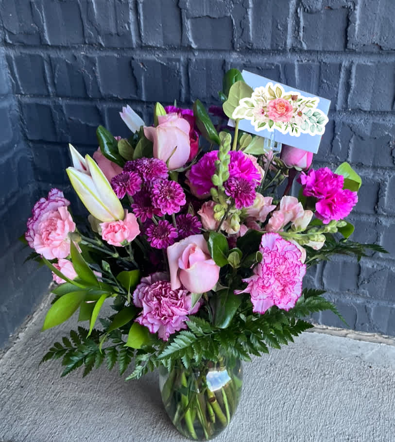 Pink and purple bouquet in a glass vase with a floral card