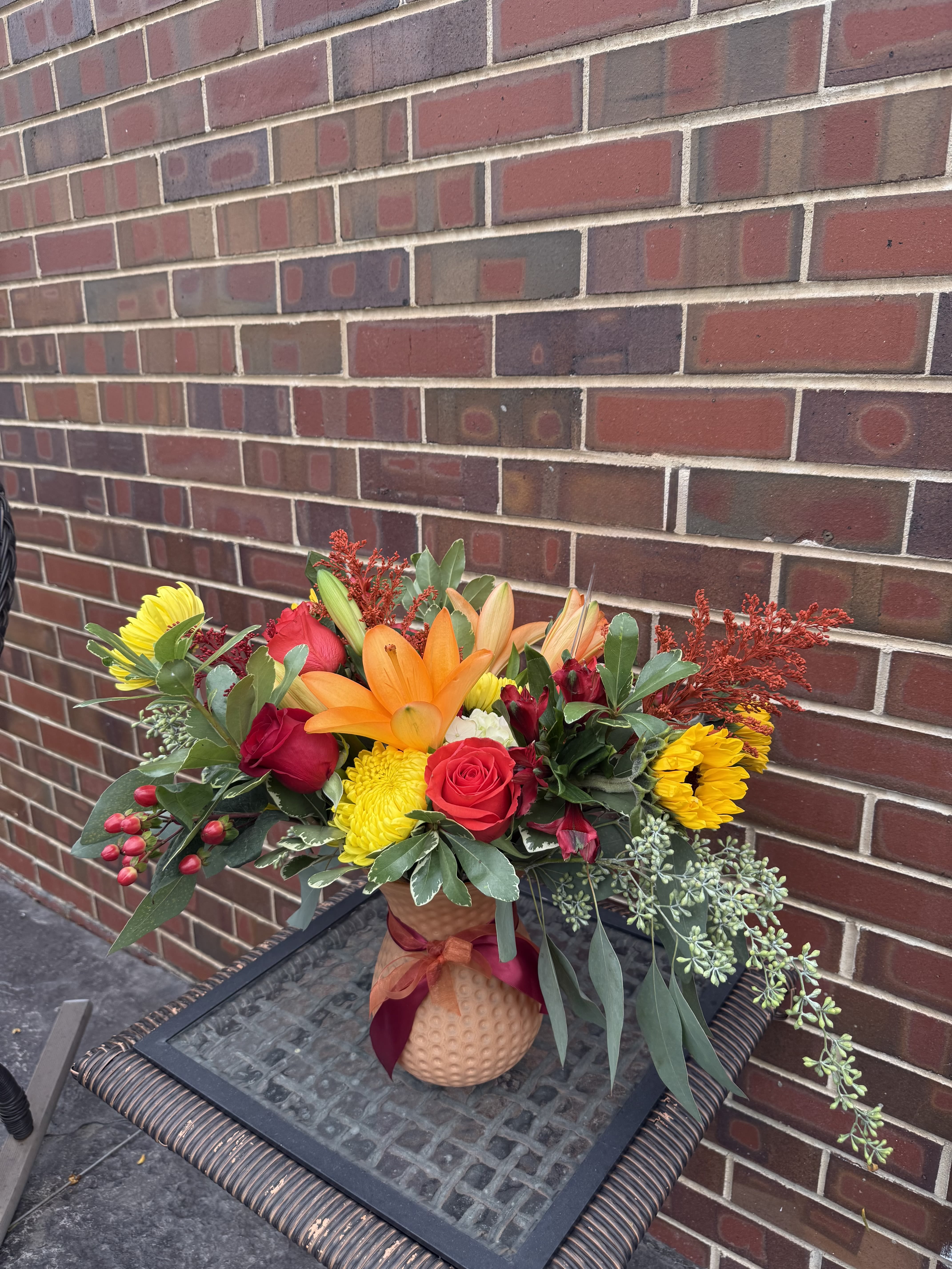Mixed bouquet in a textured vase with red, yellow, and orange flowers