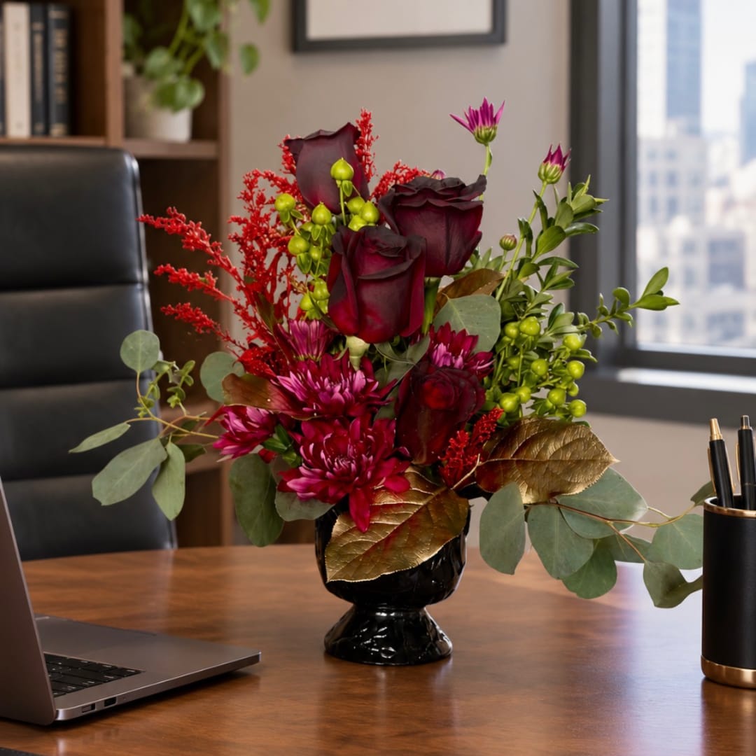 Dark red roses and magenta flowers in a black vase on a desk